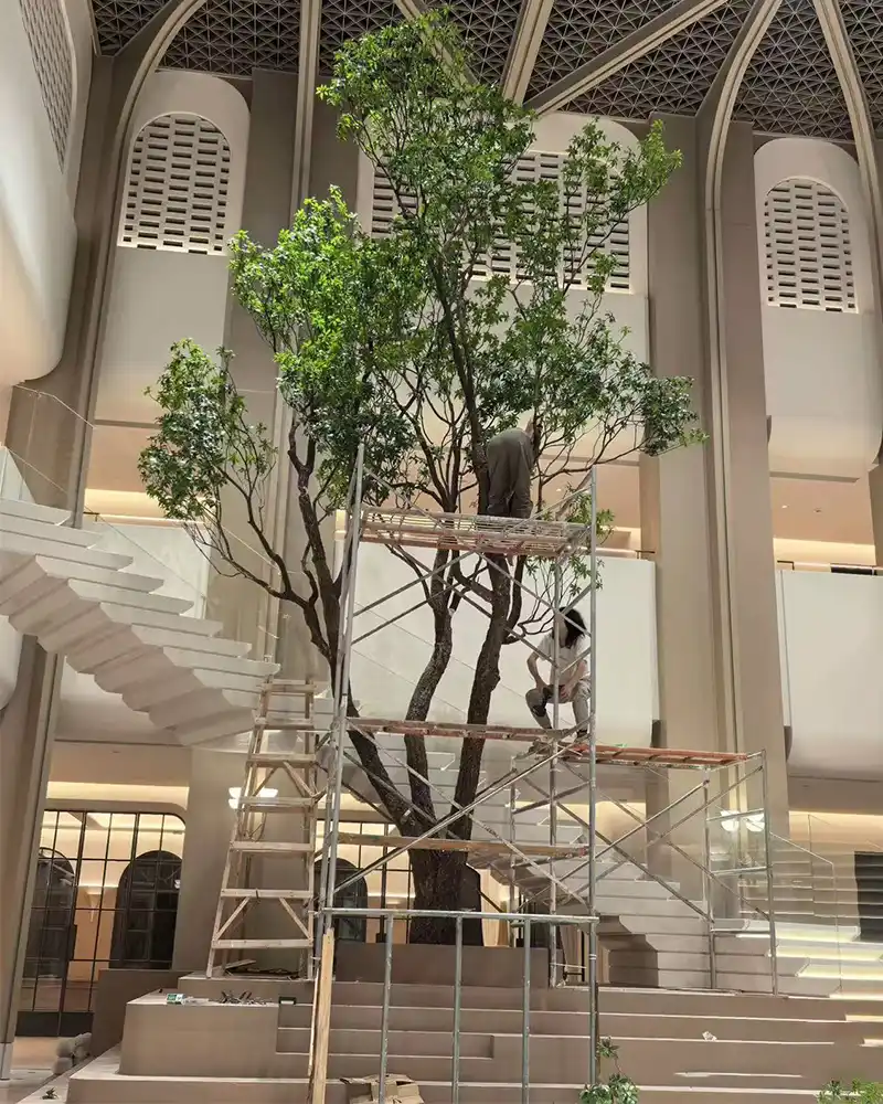 Workers on scaffolding hand-assembling fire-retardant artificial foliage for a large commercial indoor tree.